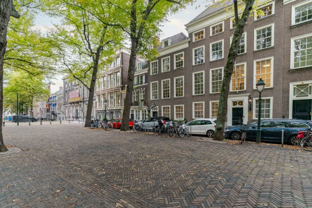 Geplaveide straat met klassieke herenhuizen, fietsen en geparkeerde auto's aan het Lange Voorhout in Den Haag.